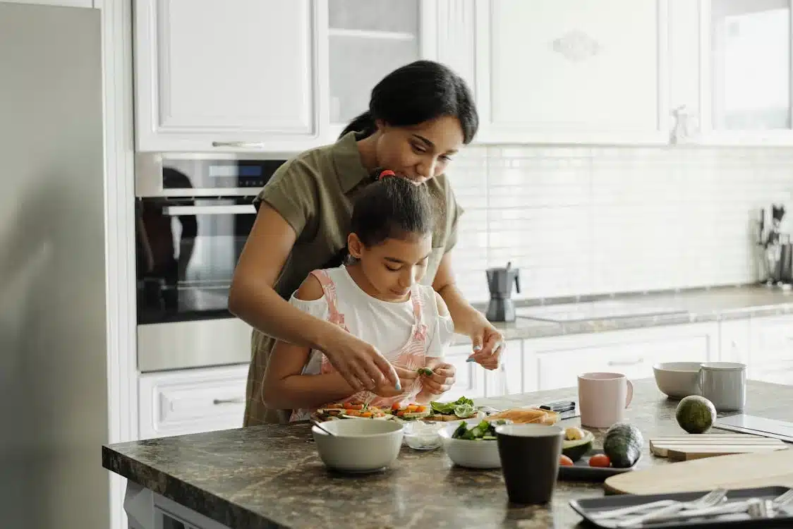Mother and Daughter Cooking Together in Kitchen – Family Recipe Moments Mother teaching daughter to prepare a healthy meal in a bright, modern kitchen — a heartwarming moment that reflects family traditions, home cooking, and the love behind every recipe.