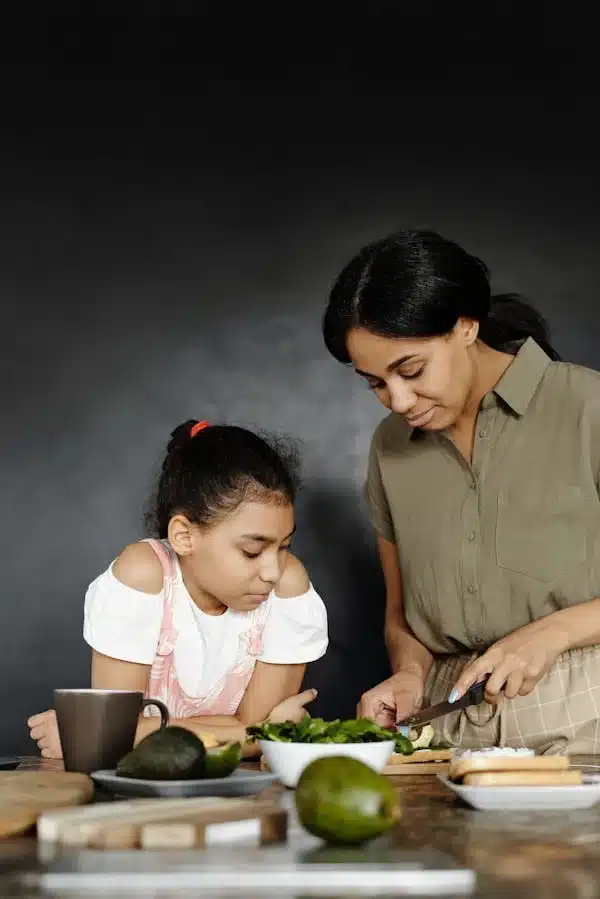 nancy-mccarthy-teaching-her-doughter-to-cook Nancy McCarthy teaching her daughter how to cook, slicing greens together at the kitchen counter — highlighting her passion for family, food, and passing down culinary traditions.